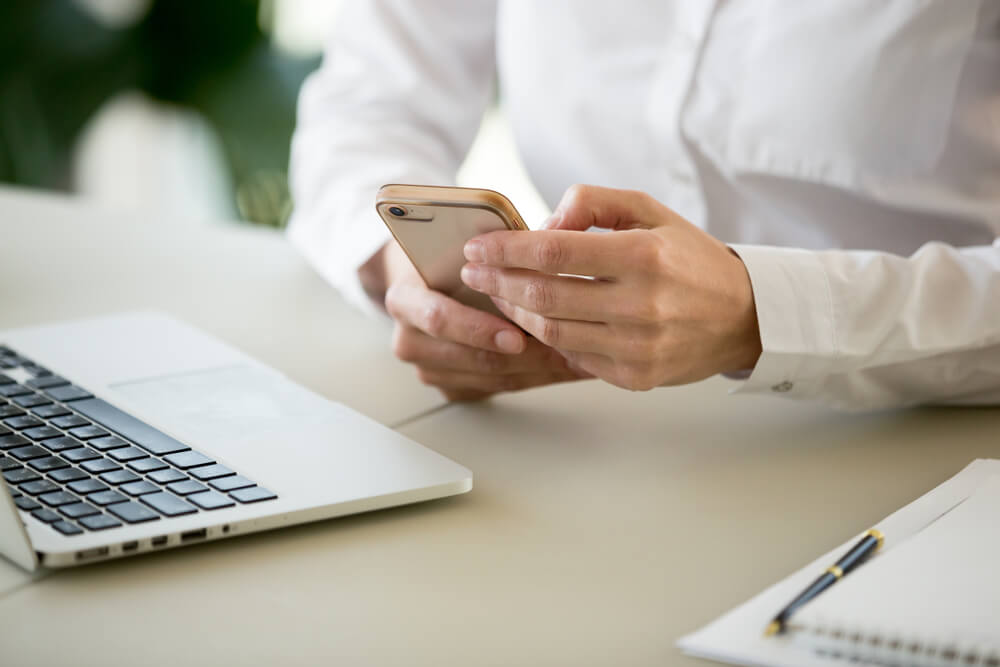 Businesswoman Using Business Applications On Smartphone In Office With Laptop